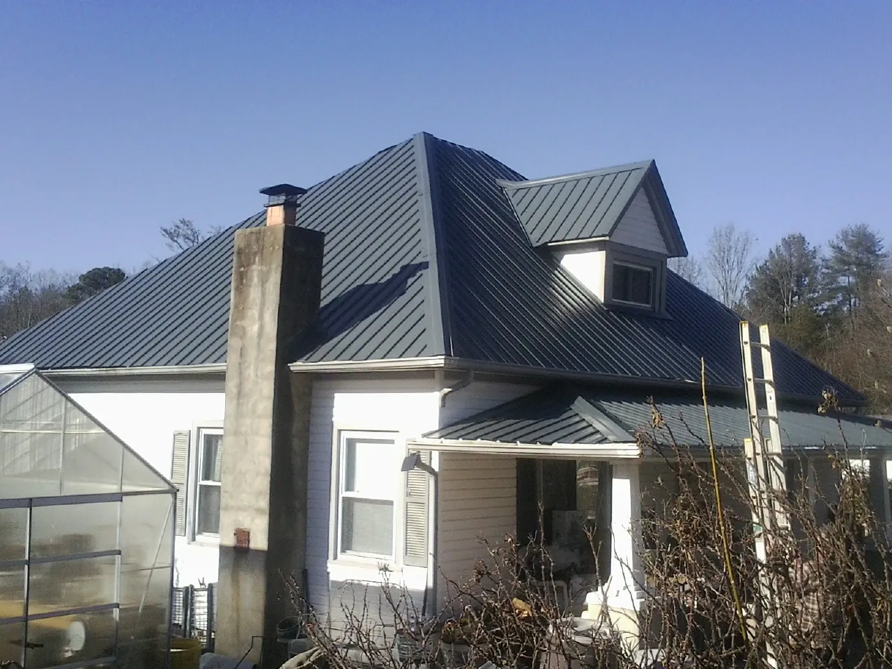 Dark blue standing seam metal roof on a white farmhouse with dormer — Slate & Tile Roof Repair by Roofing Brothers in Tivoli