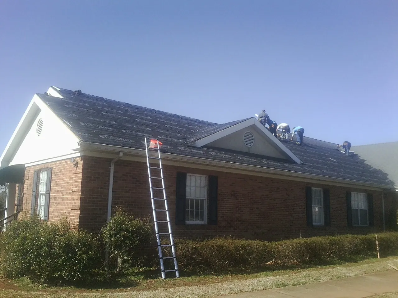 Crew tearing shingles off a brick ranch roof with a ladder set — Metal Roof Repair work by our crew in Tivoli