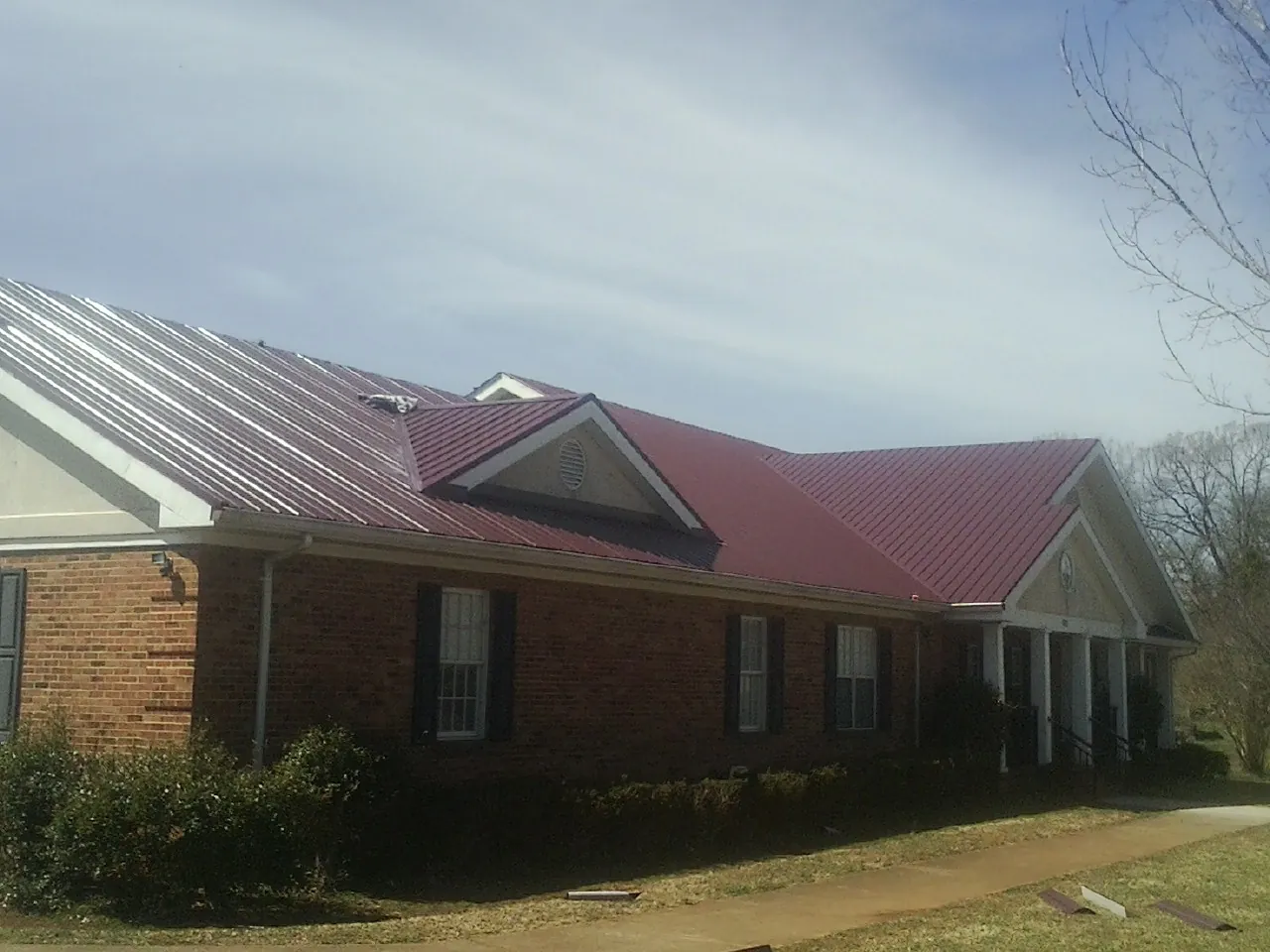 Red metal roof with gabled entries on a long brick building, from a Hail Damage Roof Repair job in Tivoli