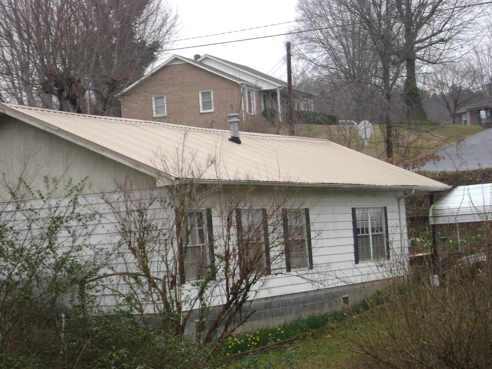 Tan metal roof on a white sided house set into a hillside — Commercial Roofing by Roofing Brothers in Tivoli